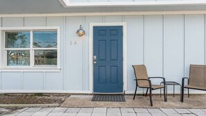 Un immeuble avec une porte bleue, le numéro « 5A » au-dessus, et deux chaises à l’extérieur.