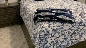 Une chambre à coucher comprenant un lit, deux tables de chevet, un ventilateur de plafond et une œuvre d’art encadrée accrochée au mur.