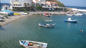 Un village côtier où des bateaux sont amarrés le long de la rive, avec une plage rocheuse et des bâtiments aux toits couverts de tuiles rouges.
