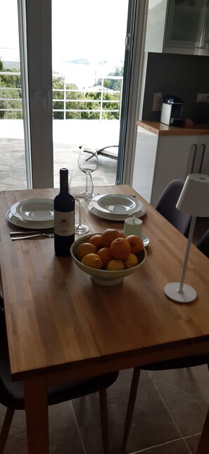 Una mesa de comedor con una botella de vino, una copa, platos y un bol de fruta.