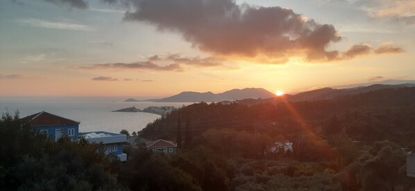 A coastal landscape with a sunset, houses, and hills in the background.
