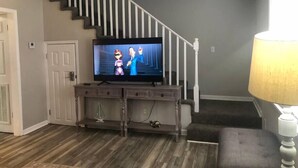 A living room with a staircase, a television, and a lamp. - Townhomes Near the Bay - #1 (Grand Bay)