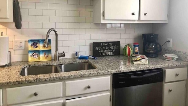 A kitchen with white cabinets, a granite countertop, a coffee maker, and a sign that reads "I like my cream & sugar with a touch of coffee." - Townhomes Near the Bay - #1 (Grand Bay)