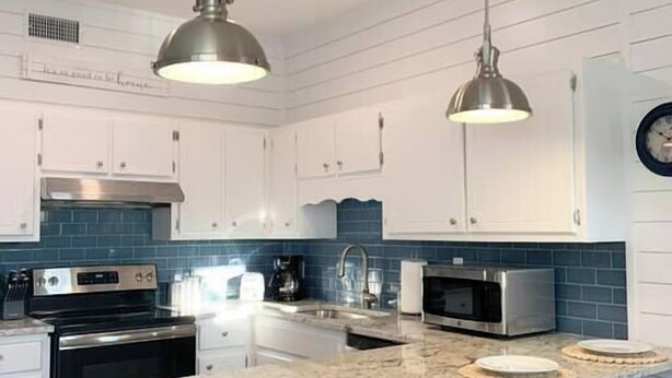 Une cuisine moderne avec des meubles blancs, un dosseret bleu, des appareils en acier inoxydable et un îlot central doté de tabourets.