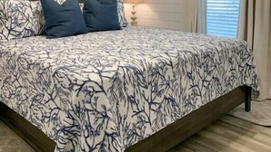 Une chambre à coucher avec un lit, une table de chevet, une lampe et une fenêtre avec des rideaux.