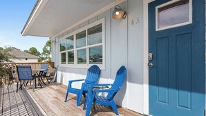 Une maison avec une porte bleue, une terrasse dotée de meubles d’extérieur et une fenêtre avec des stores.