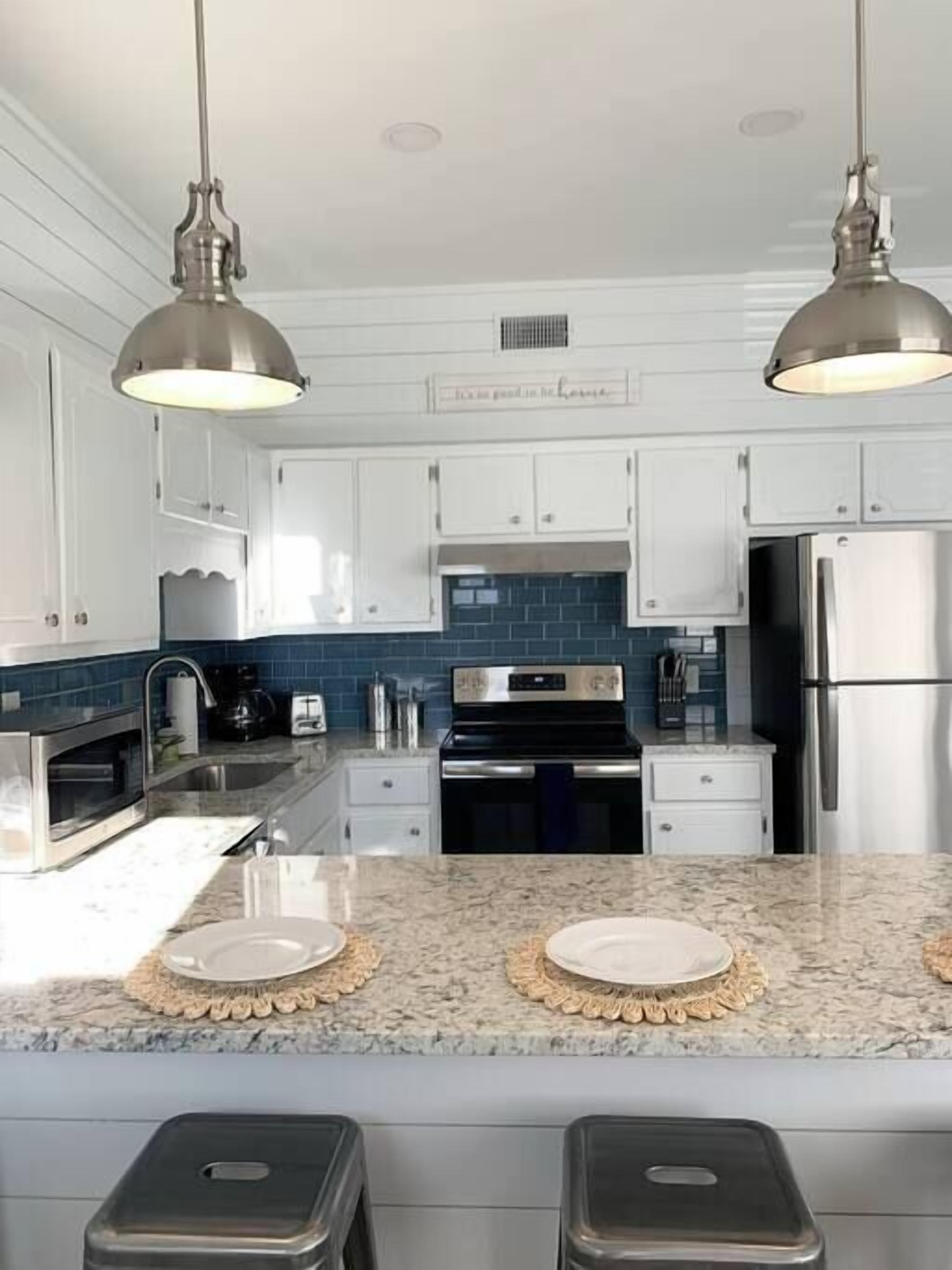 A modern kitchen with white cabinets, a black stove, stainless steel appliances, and two pendant lights.