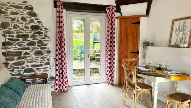 A room with a stone wall, a wooden door, a dining table with chairs, and a view through a glass door. - La Haye D'armor, Gite au Calme à la Campagne, Animaux de Compagnie Acceptés! (Le Mené)