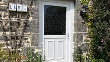 Un bâtiment en pierre avec une porte blanche, une enseigne en bois sur laquelle on peut lire « LENID », et un petit jardin agrémenté de fleurs et de plantes.