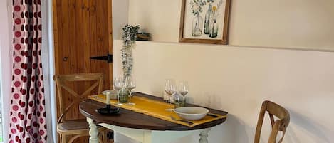 Un coin repas avec une table en bois, deux chaises, une estampe botanique encadrée et un rideau à motifs à pois.