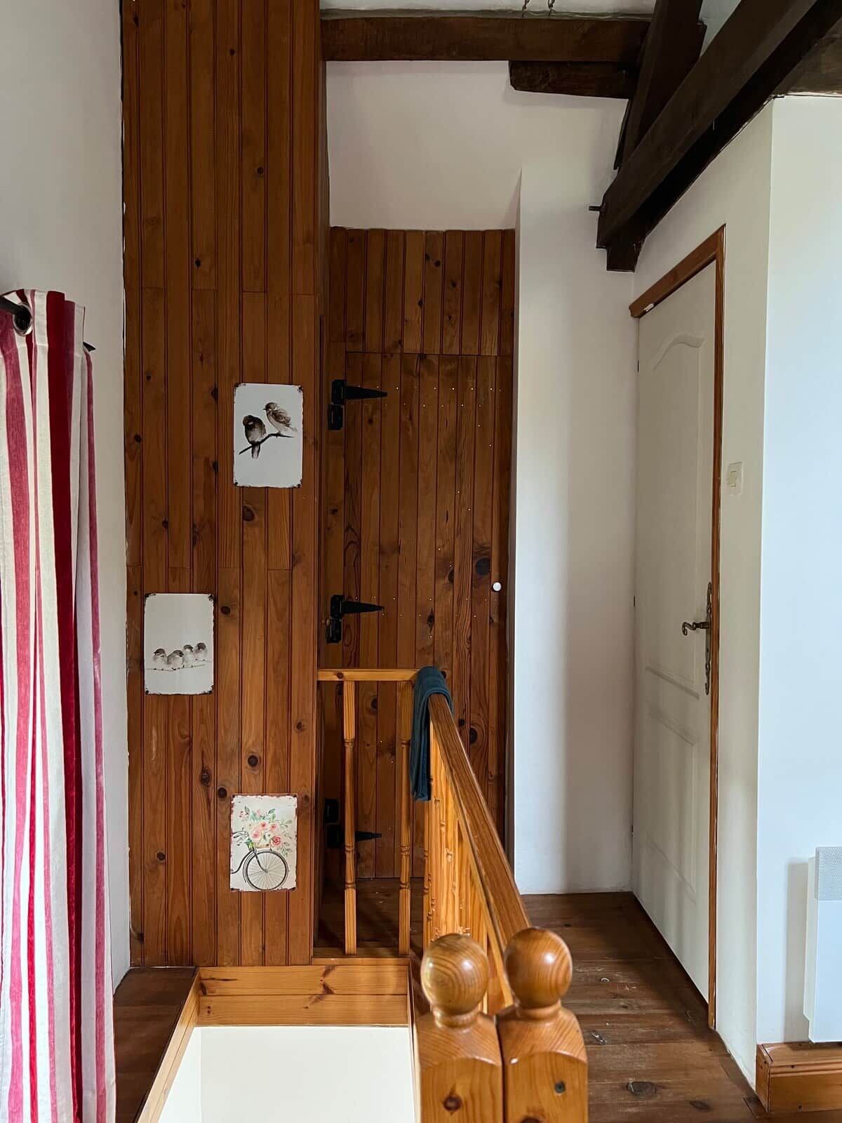 Un escalier en bois avec une rampe, une porte avec une poignée et un mur orné de tableaux encadrés.