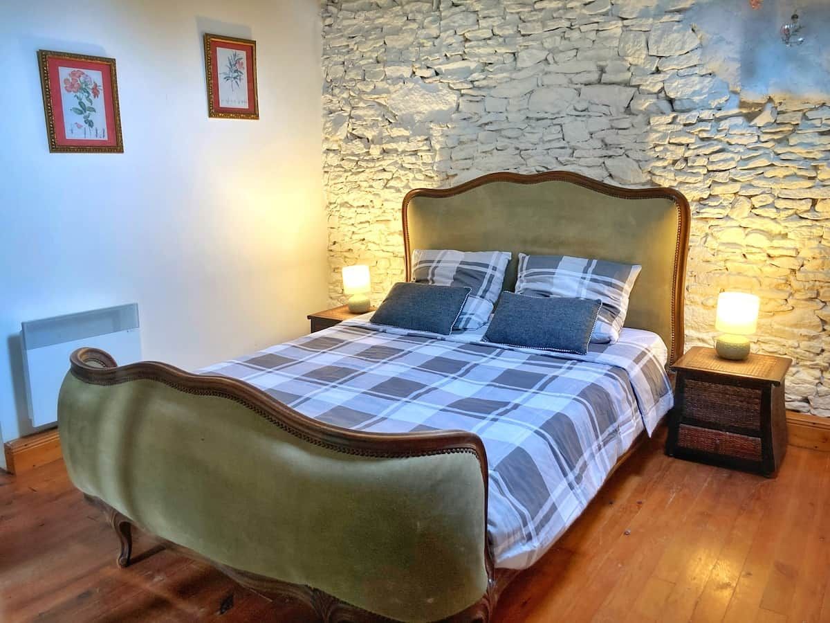 A bed with a plaid bedspread and two pillows, a stone wall, and two framed pictures on the wall.