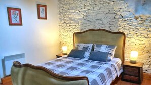 A bed with a plaid bedspread and two pillows, a stone wall, and two framed pictures on the wall. - La Haye D'armor, Gite au Calme à la Campagne, Animaux de Compagnie Acceptés! (Le Mené)