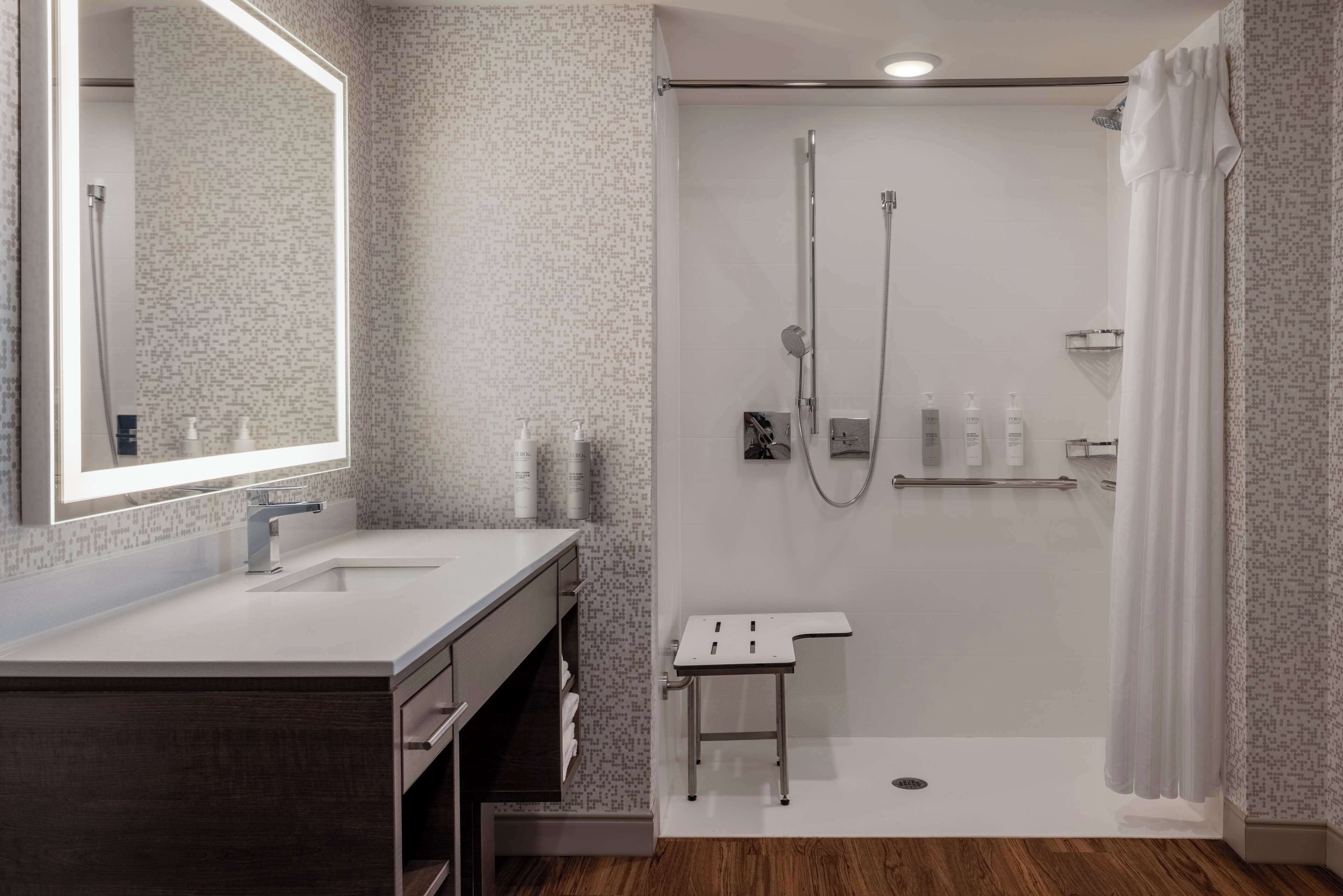Une salle de bain moderne avec une douche, un meuble-lavabo avec un miroir et un petit tabouret.