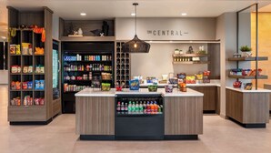 Un espacio comercial moderno con una isla central llena de bebidas, rodeada de estantes con aperitivos y productos envasados.
