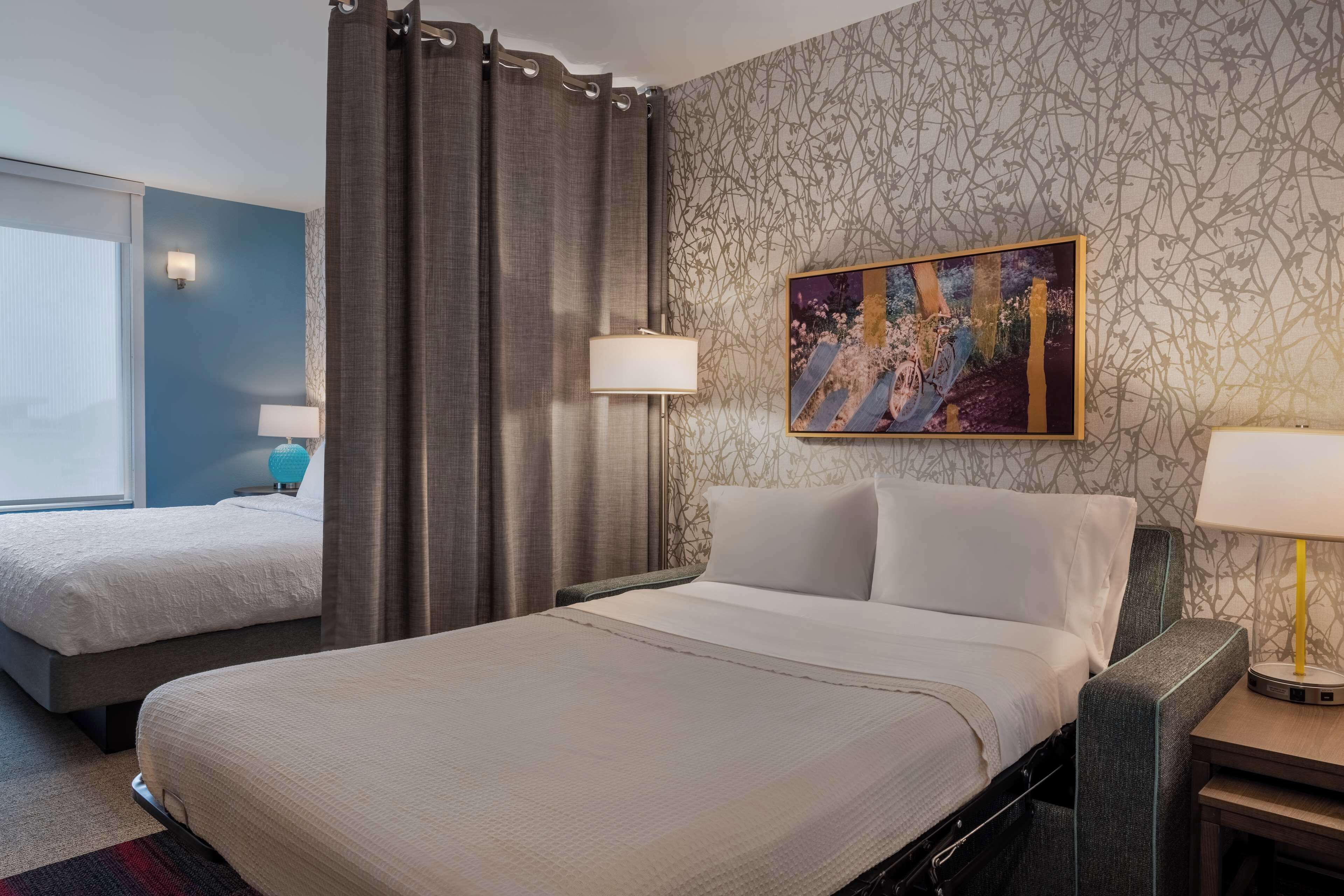 A hotel room with two beds, a large painting, and a patterned wall.