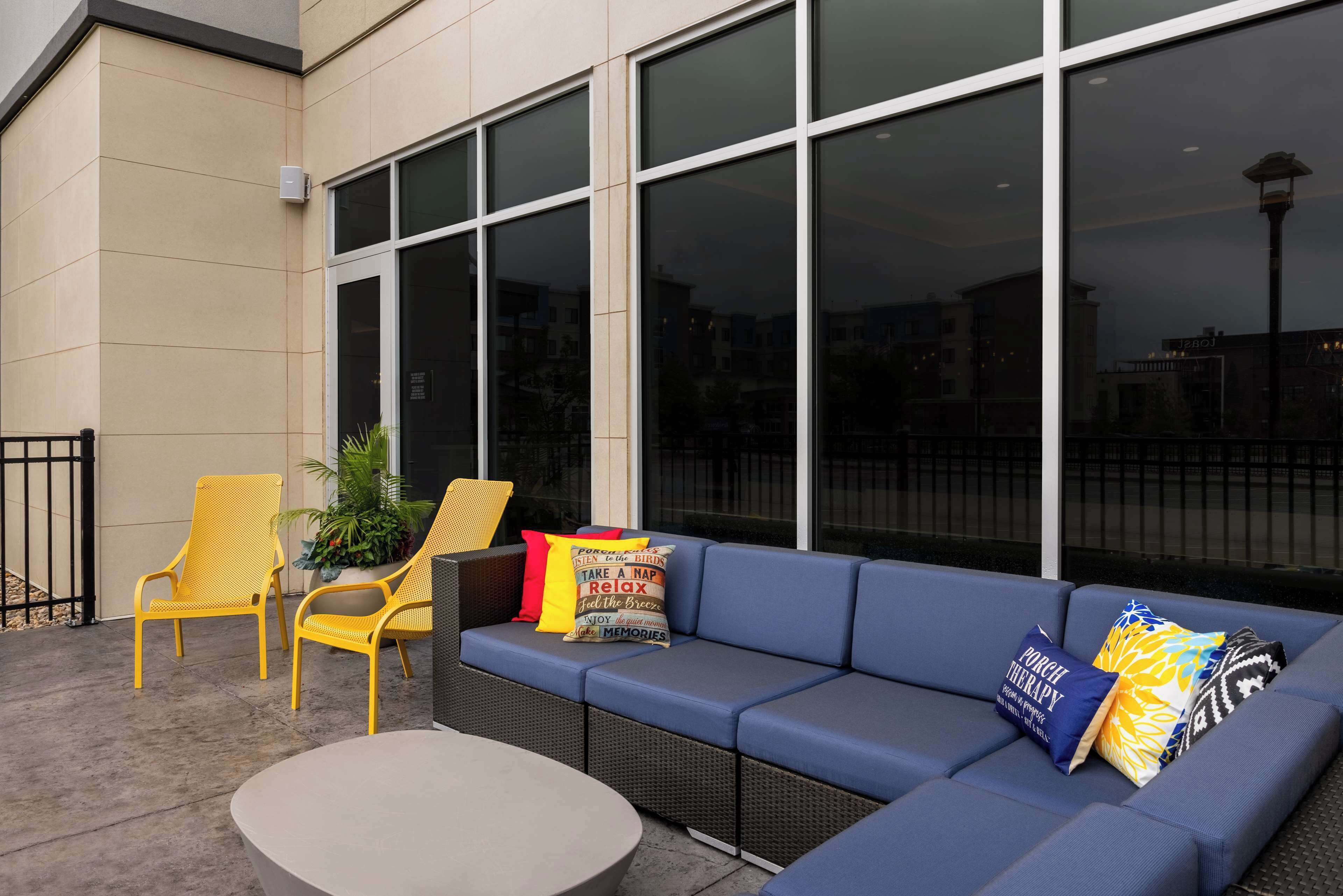 An outdoor seating area with a blue sofa, yellow chairs, and a round table.