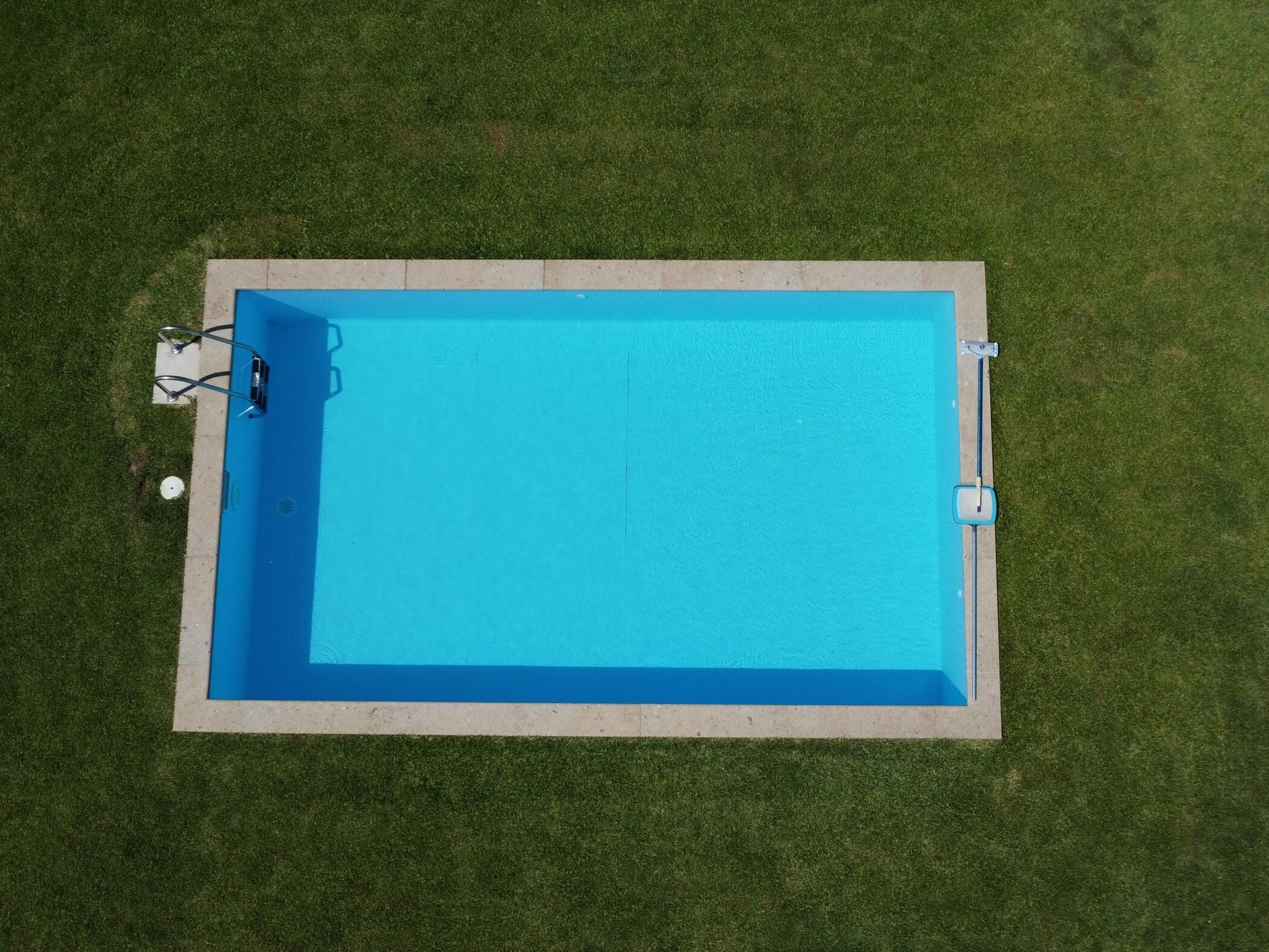 A rectangular swimming pool with a blue interior, surrounded by a concrete deck and bordered by grass.