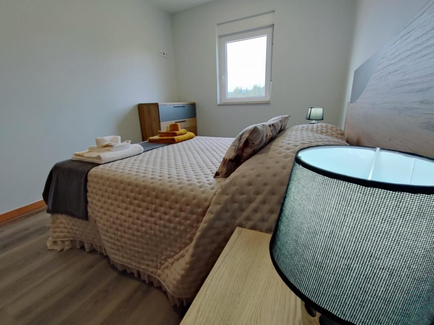 A bedroom with a bed, bedside table, lamp, and a window.