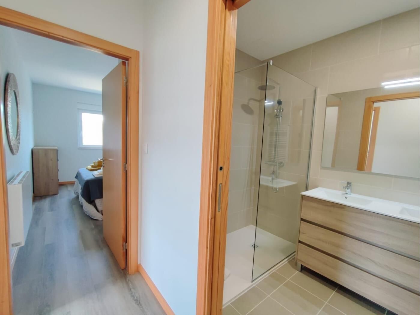 Ein modernes Badezimmer mit Duschkabine aus Glas, Waschtisch aus Holz und einem großen Spiegel.
