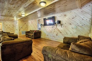 A cozy room with wooden walls and floors, a flat-screen TV mounted on the wall, and several plush sofas arranged for seating.
