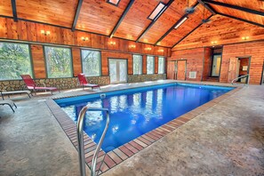 An indoor swimming pool with wooden walls and a stone accent wall, surrounded by red chairs.