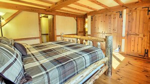 A bedroom with a wooden bed frame, a plaid bedspread, and a wooden ceiling with exposed beams.