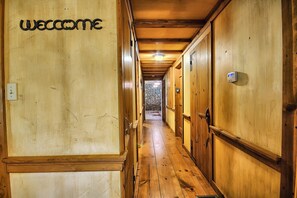 Ein Holzboden-Flur mit einem 'Welcome'-Schild, Holztüren und einer Steinwand am Ende.