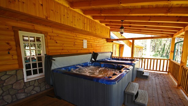 A wooden cabin with a hot tub, stone wall, and wooden deck.