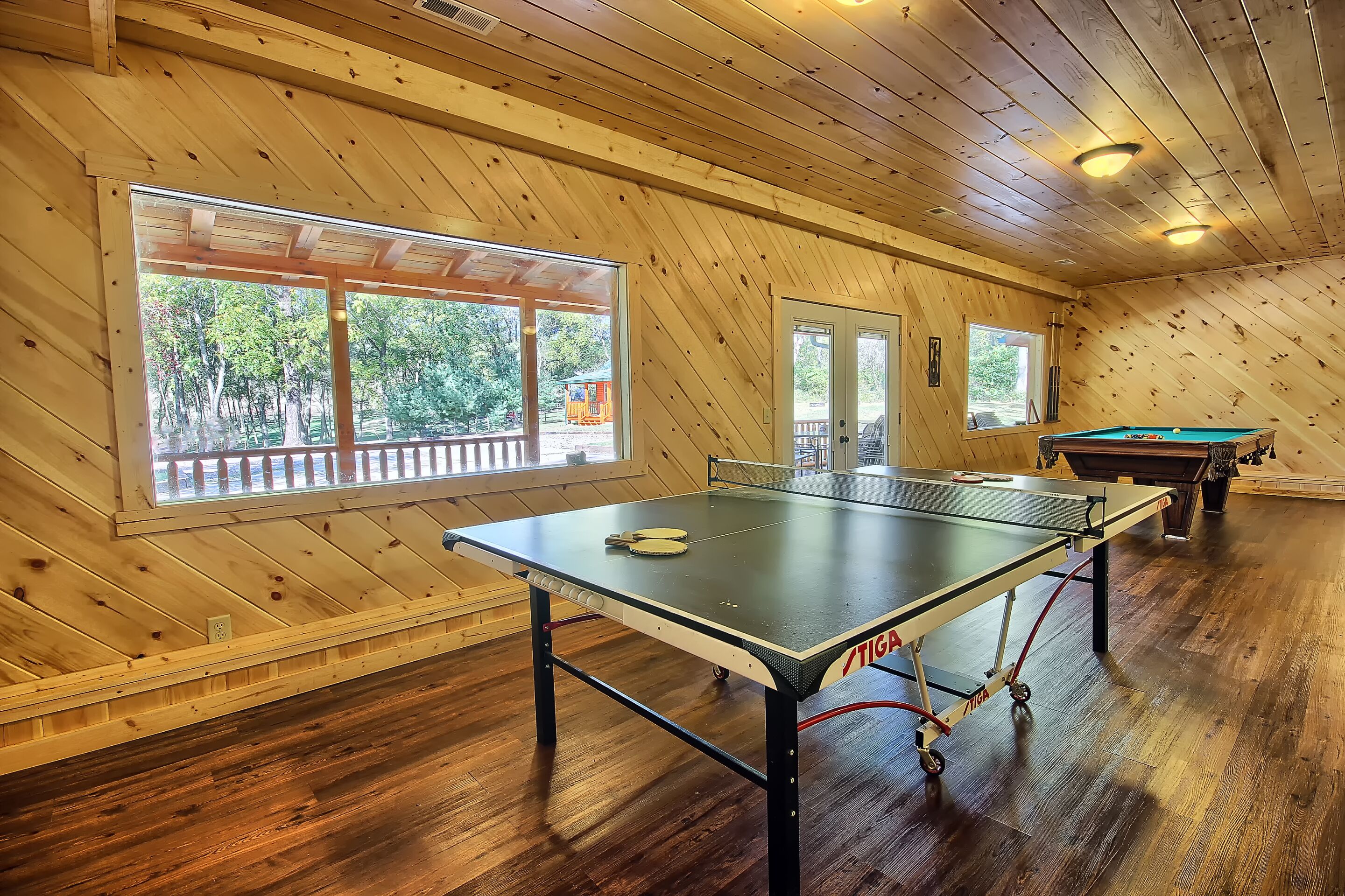 Une pièce équipée d’une table de ping-pong, d’une table de billard et de grandes fenêtres donnant sur l’extérieur.