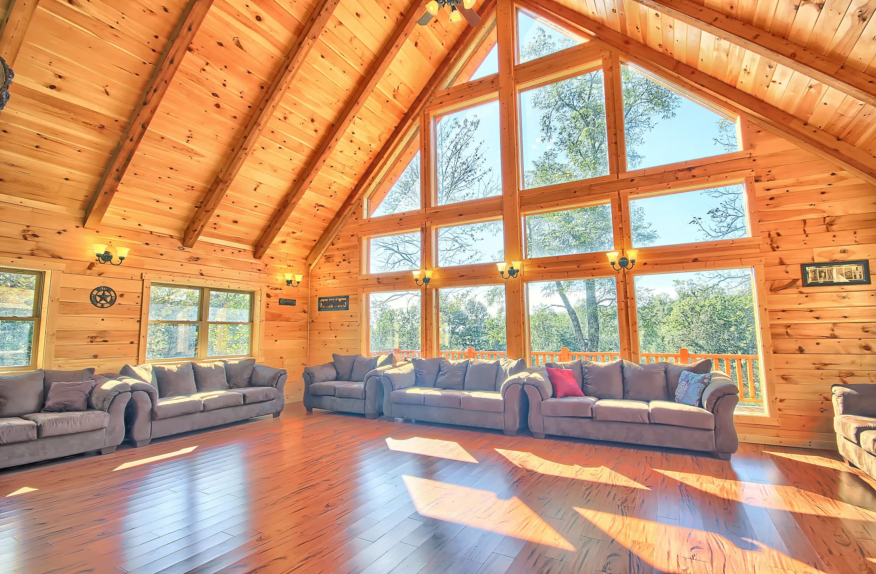 A spacious room with a high ceiling and large windows, furnished with multiple sofas and a wooden floor.