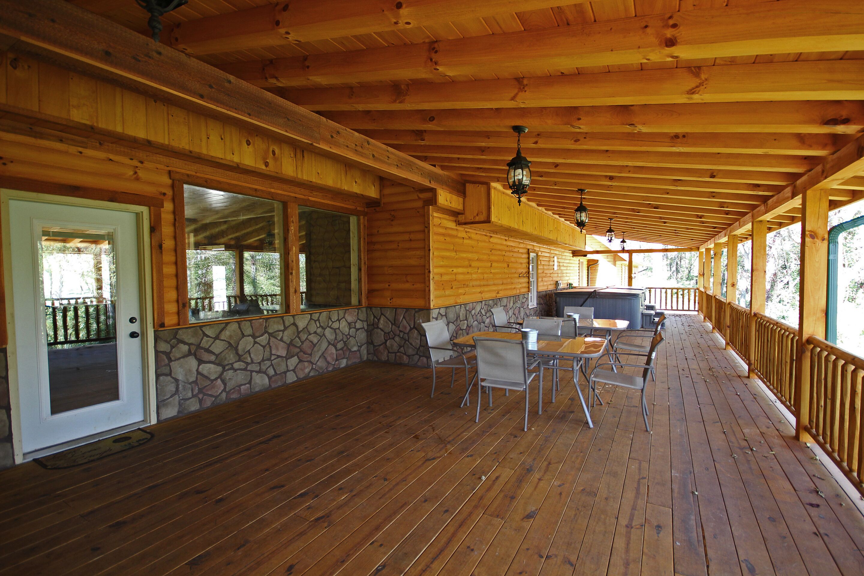 A covered outdoor patio with wooden flooring, stone accents, and a seating area with tables and chairs.