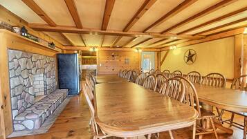 A large wooden dining table with chairs, a stone wall, and a kitchen in the background.