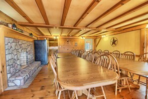 Ein großer Holzesstisch, umgeben von Stühlen, einer Steinsitzbank und einem Kamin aus Stein.