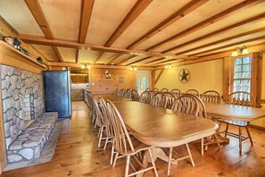 A long wooden dining table surrounded by chairs in a rustic room with stone walls and wooden beams. - Western Lodge - Huge, w/Heated Pool, Hocking Hills (Logan)
