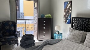 A bedroom with a bed, a chair, a nightstand, a dresser, and a view of a balcony.