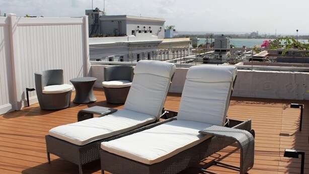 A rooftop terrace with two lounge chairs, a small round table, and a white partition.