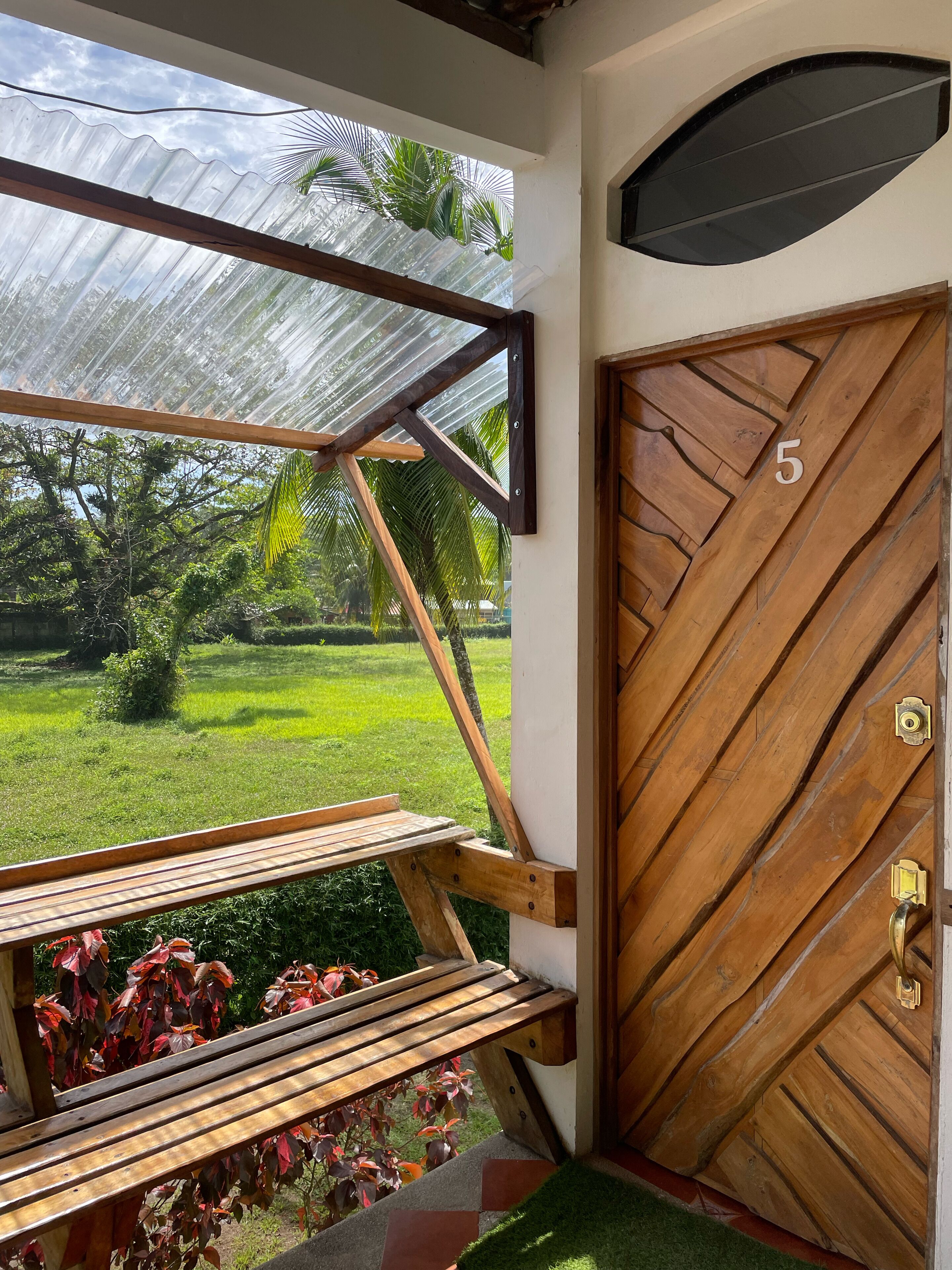 A wooden door with a number '5' and a metal handle, a wooden bench, and a glass door frame with a view of a green landscape.