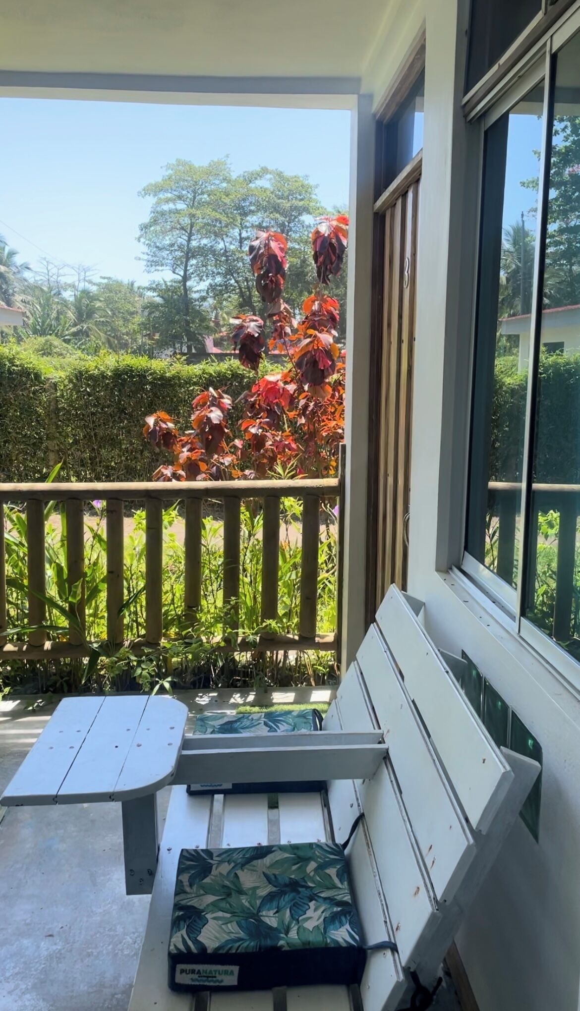 Un balcon avec un banc blanc, une table et une vue sur les arbres et le feuillage.