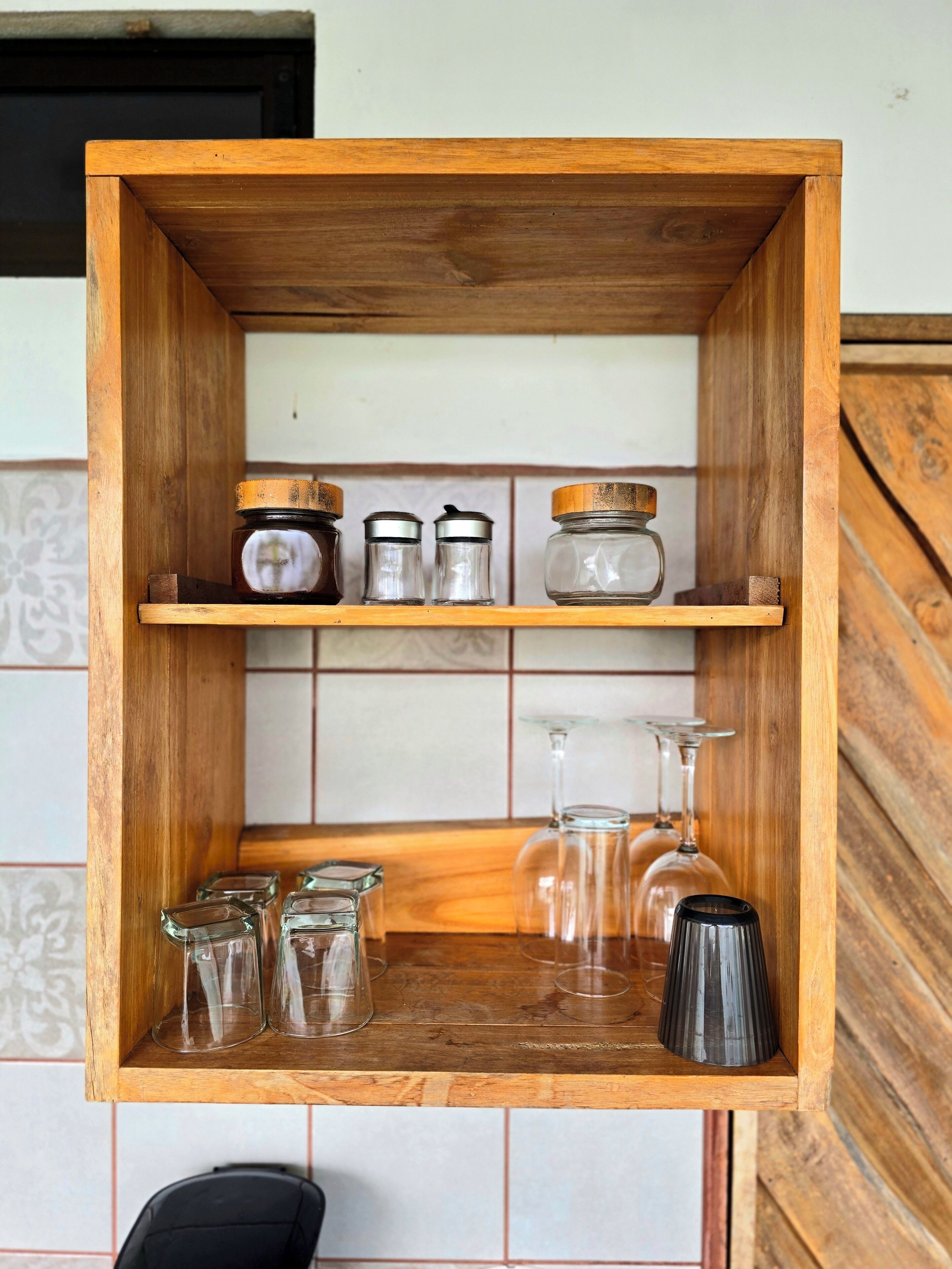 A wooden shelf unit with glass jars and wine glasses.