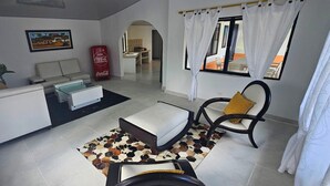 Una sala de estar moderna con un sofá, una mesa de centro, un tapete estampado y un área de comedor al fondo.