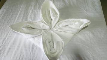 A neatly folded white towel on a bed with a white quilted bedspread.
