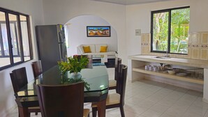 Una cocina moderna con comedor, que incluye una mesa de vidrio, sillas, un refrigerador, una estufa y una ventana con vistas a la vegetación.