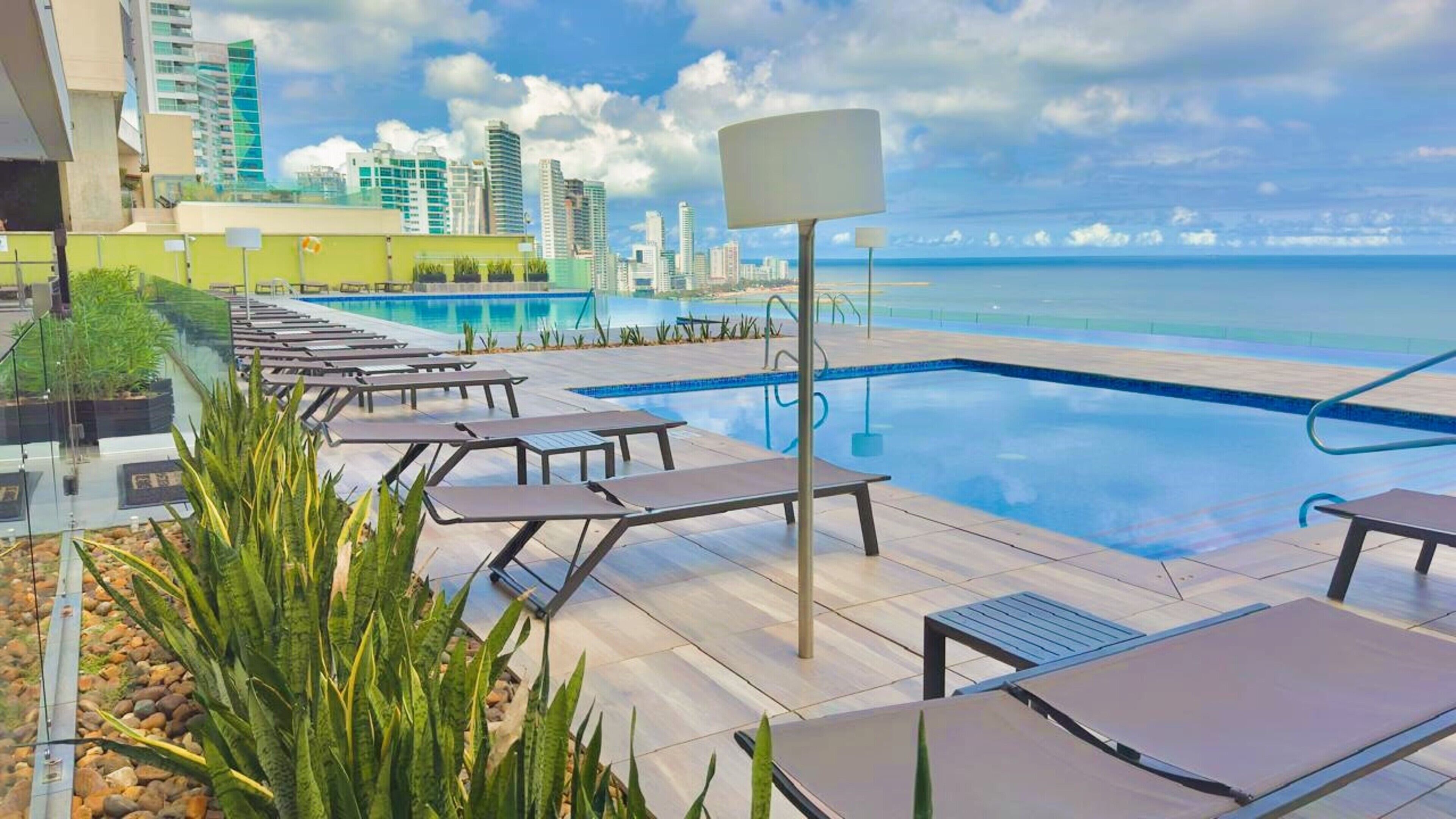 A rooftop pool with lounge chairs and a city skyline in the background.