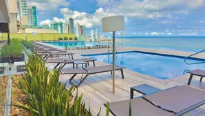Una piscina en la azotea con sillones de descanso y un horizonte urbano al fondo.