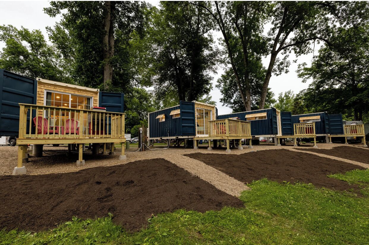 A row of modular cabins with wooden decks and windows, surrounded by trees.