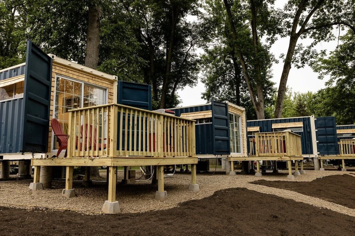 Portable cabins with openable windows and a wooden deck, surrounded by trees.