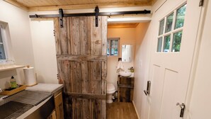 Un baño con puerta de madera rústica, un lavamanos con un tendedero y un inodoro.