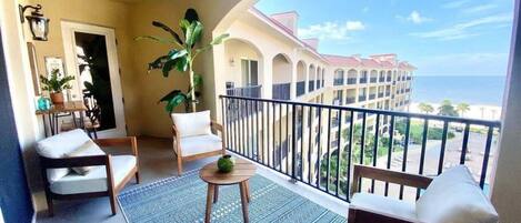 A balcony with a view of the ocean, a patterned rug, and two chairs.