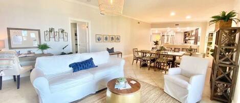 Un salon avec un canapé blanc, une table basse ronde et un coin repas comprenant une table et des chaises en bois.